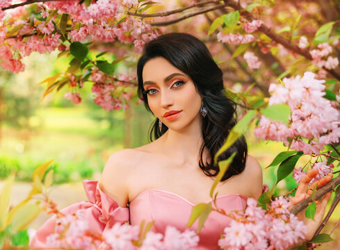 Portrait Fantasy girl princess in blooming spring garden flowers sakura tree green grass. Happy woman queen beauty face Lady in romantic pink sexy dress bare open shoulders vintage old style art photo