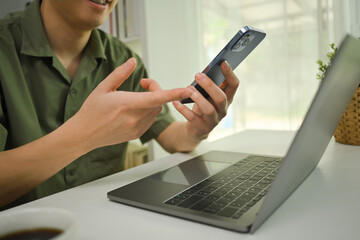Man sitting at desk with laptop and using smartphone, communicating online or distantly working at home