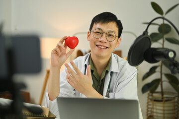 Smiling male doctor recording video blog for educating about heart disease. Healthcare, medicine and blogging concept