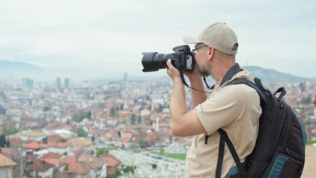 A professional photographer taking pictures of the city of Sarajevo from a viewpoint using a DSLR camera.