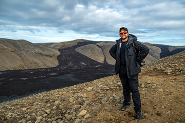 Fototapeta premium man with backpack and in sunglasses posing with lava field at icelandic Fagradalsfjall volcano valley on background