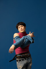 Uniqueness. Portrait of stylish young guy posing in pants on hands, pink singlet and jeans, posing against blue studio background. Concept of men's fashion, extraordinary style, art, beauty, trends