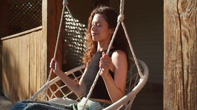 happy young female riding on macrame swing chair in country house outdoors