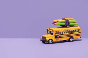 School bus with with pencils and pens on top on lilac purple background. Back to school. Delivery...