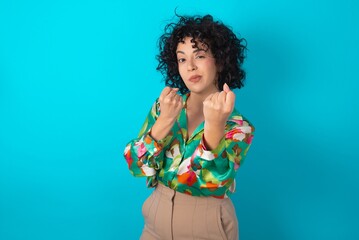 young arab woman wearing colorful shirt over blue background Ready to fight with fist defense gesture, angry and upset face, afraid of problem.