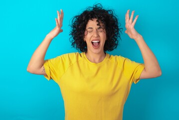 young arab woman wearing yellow T-shirt over blue background goes crazy as head goes around feels stressed because of horrible situation