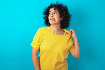 young arab woman wearing yellow T-shirt over blue background stressed, anxious, tired and frustrated, pulling shirt neck, looking frustrated with problem