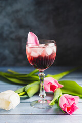 Pink cocktail with champagne or prosecco and ice in crystal wine glass and white and white tulips