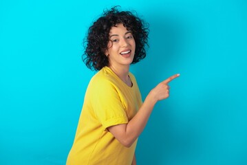 Profile photo of young arab woman wearing yellow T-shirt over blue background indicate finger empty space offer