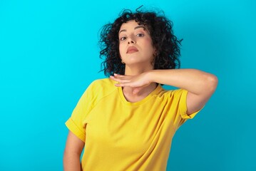 young arab woman wearing yellow T-shirt over blue background cutting throat with hand as knife,...