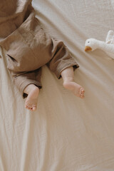 Top view of newborn baby lying on bed. Cute cozy linen bodysuit, toy duck. Little baby fashion...