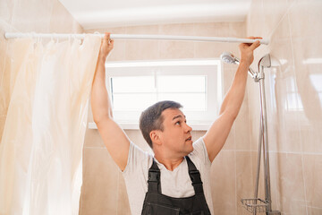 A masterinstalls the shower curtain bar in the bathroom. 