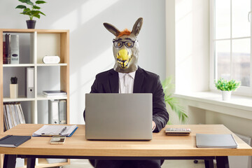 Funny business man and company employee wearing suit and animal donkey mask sitting at the desk on...