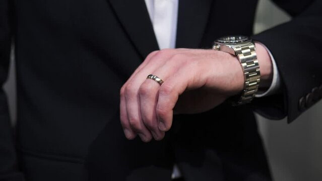 Closeup unrecognizable man with wedding ring looking at wrist watch in jewerly store. Male person in formal modern suit checking time indoors. Guy hiding watch under sleeve, puts his hand down.