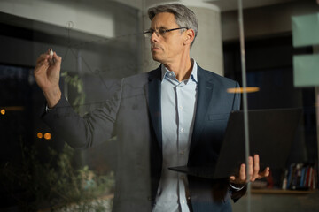 Portrait of successful businessman in office. Man writing on the glass board in office.