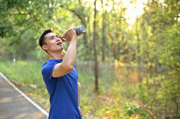 Thirsty and tired Asian male runner in sportswear drinks water from a bottle while running