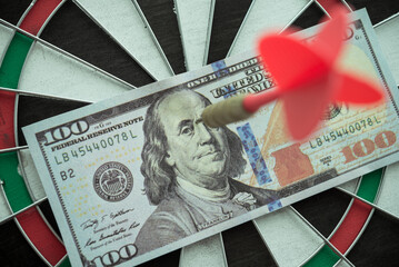 Red arrow dart hit US dollar banknote bill at center of dartboard background. Successful and...
