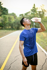 Thirsty and exhausted male runner drinks water from a bottle while running in a park