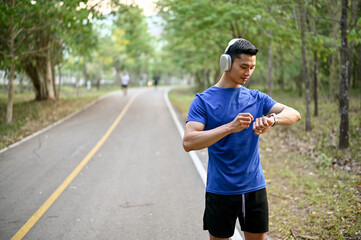 Handsome Asian man wearing headphones, checking his running miles on his smartwatch