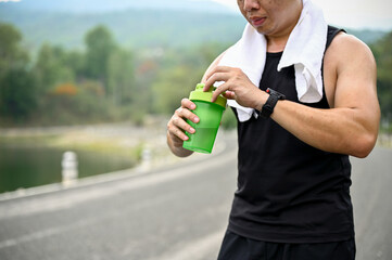 Cropped image, Sweaty and thirsty mature Asian man drinks water after running