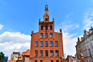 Old architectural building made of red bricks, windows and a tower at the top with forged elements. Sunny summer day with blue sky.  Poland, Poznan, June 2022
