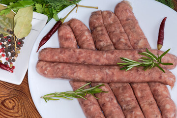 Raw sausages among spices and greens on dish close-up