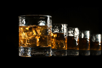 Five glasses of Scotch whiskey with ice stand in a line towards you on a black background