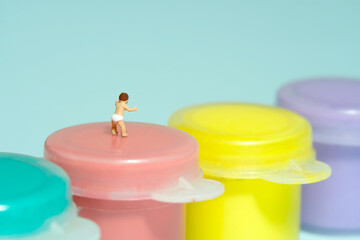Miniature tiny people toy figure photography. Art study and learning concept. A boy toddler standing above paint tube. Isolated on blue background