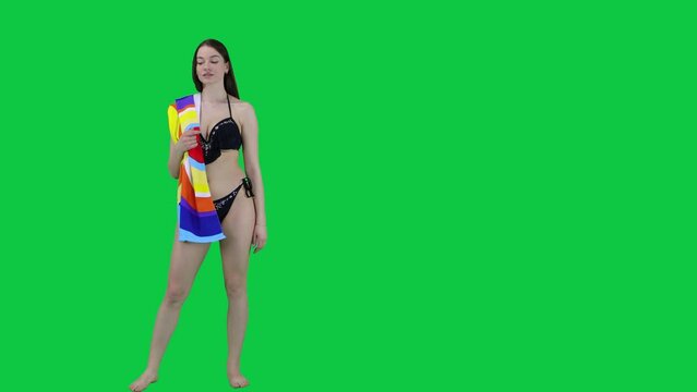An attractive Caucasian model walking in a bikini and towel looking for a spot in front of a green screen