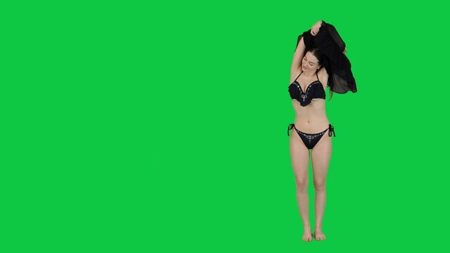 Beautiful female model takes off her dress to reveal bikini in front of a green screen