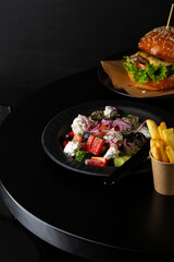 Greek salad on black table potatoes and burger