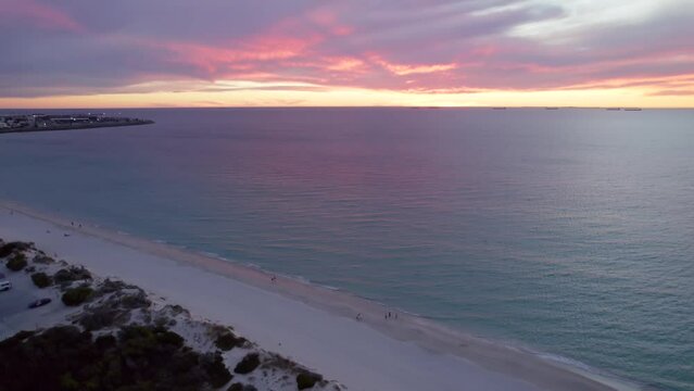 An aerial shot of Port Beach at sunset in Perth, Western Australia. People walk across the beach and watch the sunset.