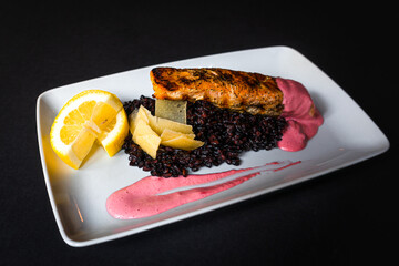 Grilled salmon served on a bed of black rice and pink sauce 