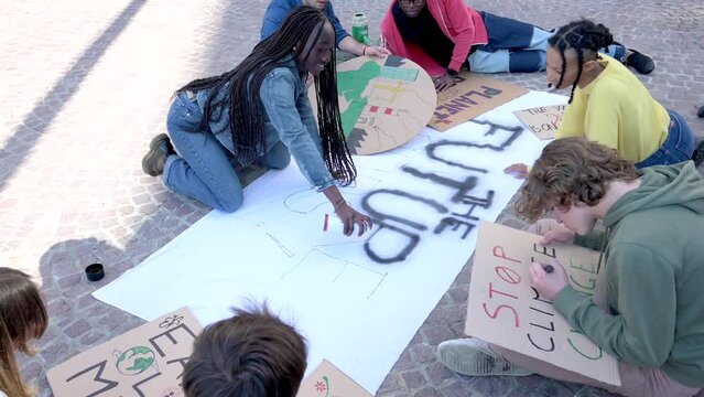 Young African girl writes a slogan on a sheet with spray paint, activists for respect and protection of the environment are organizing in protest