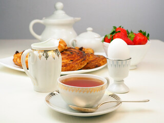 Breakfast with egg, tea, milk, buns, strawberry on white table