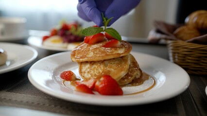 Close-up of a hand putting a mint leaf on pancakes. The chef prepares breakfast in the hotel room. Cook's hands put mint leaves on pancakes.