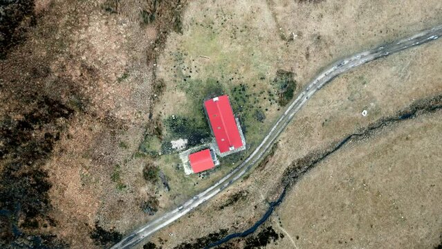 A drone slowly rises above the red roof of a remote bothy (mountain shelter) in the highlands of Scotland in winter.
