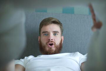 Young happy man looking at his penis under blanket, surprised guy is having good morning potency,...