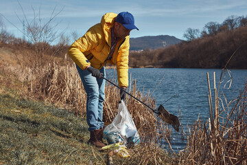 Volunteer and environmental activist cleaning dirty river shore filled with trash.