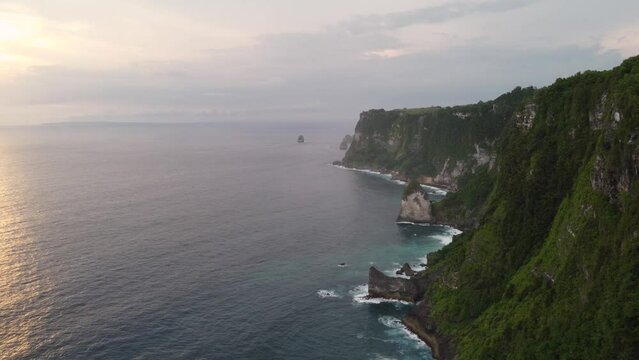 Aerial Sunset view Tropical coastline of Nusa Penida Island high steep green cape cliffs and Coves overlooking the waves of indian ocean crashing downdiamond shaped rocks, Indonesia.