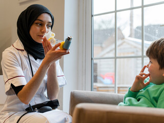 Female doctor demonstrating to boy how to use inhaler