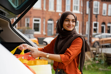 Woman wearing hijab putting shopping bags into car trunk
