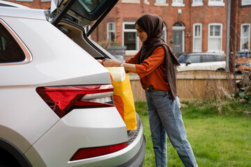 Woman wearing hijab unloading shopping bags from car trunk