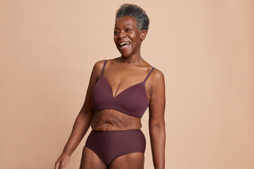 Studio shot of senior woman in underwear laughing against beige background