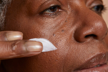 Close-up of senior woman applying face cream on cheek