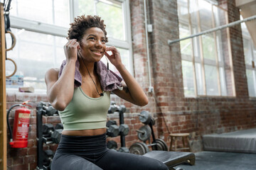 Woman putting earphones on during training on gym - obrazy, fototapety, plakaty
