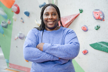 Portrait of smiling woman standing with arms crossed in front of climbing wall