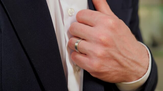 Elegant man's hand with a beautiful white gold ring places his hand on jacket collar in closeup view. This image conveys elegance, style, and attention to detail. Trend business people in formal suit.