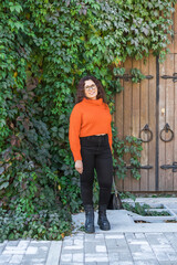 Portrait of carefree young woman smiling with big door background. Cheerful latin girl wearing eyeglasses in the city. Happy brunette woman with curly hair and spectacles smiling. Copy space and empty