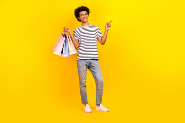 Full body picture advert brand design man direct finger empty space hold shopping bags summer sale isolated on yellow color background